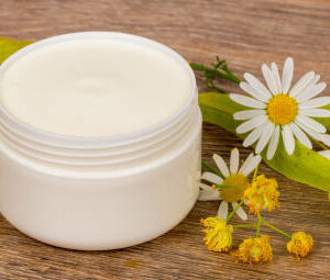 Body cream opened plastic jar with chamomile and linden flowers on wooden table