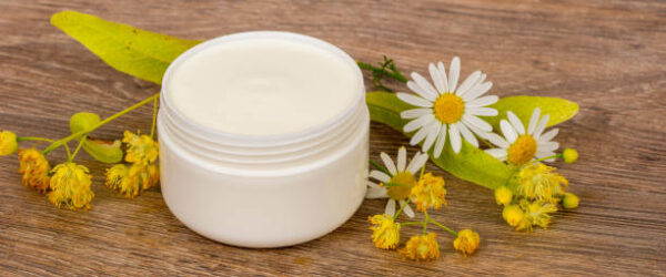 Body cream opened plastic jar with chamomile and linden flowers on wooden table